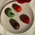 A set of three handcrafted plant-based chocolate bonbons, with distinctive flavors, placed on a plate with a backdrop of a red rose and a white plate.