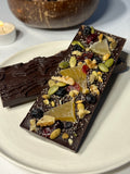 Handcrafted 64% single-origin dark chocolate bar in Infinite Pâtisserie's signature topography mold, topped with walnuts, dried mango, blueberries, cranberries, pumpkin seeds, and chia seeds.