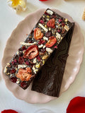 A handcrafted 64% single-origin dark chocolate bar topped with toasted pistachios, freeze-dried strawberries, candied yuzu, rose petals, cacao nibs, and flaky maldon sea salt.