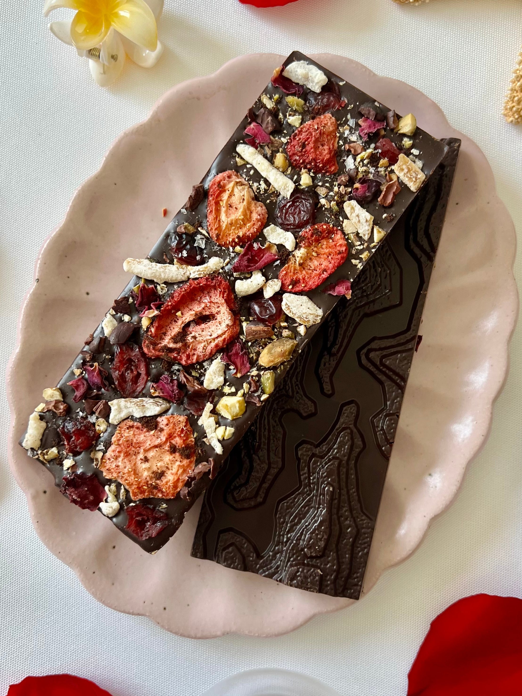 A handcrafted 64% single-origin dark chocolate bar topped with toasted pistachios, freeze-dried strawberries, candied yuzu, rose petals, cacao nibs, and flaky maldon sea salt.