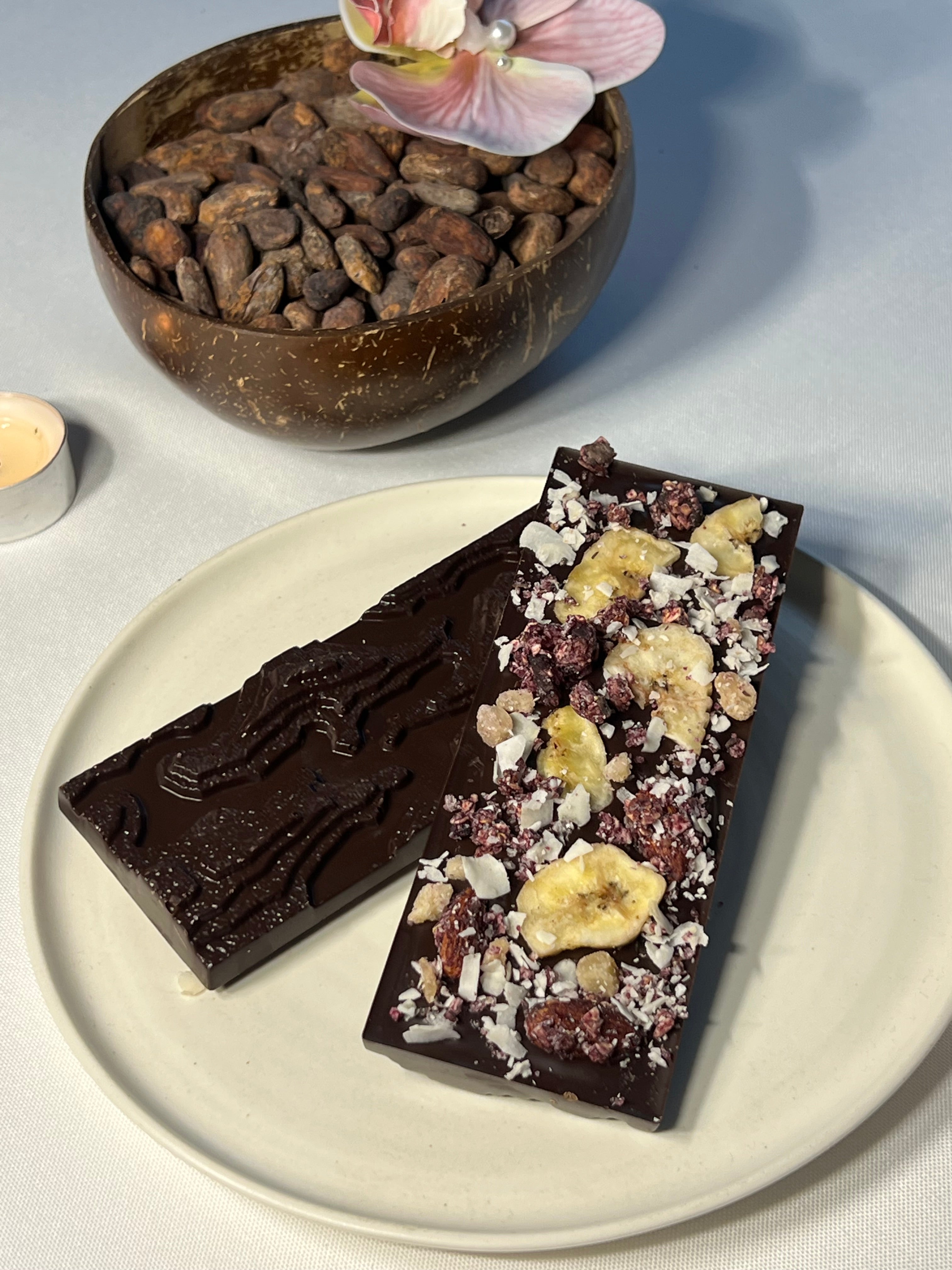 Handcrafted 64% single-origin dark chocolate bar in Infinite Pâtisserie's signature topography mold, topped with vibrant purple ube, shredded coconut, banana chips, roasted almonds, and candied ginger.